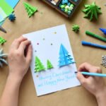 Making greeting card with origami 3D Xmas tree from paper. Merry Christmas and Happy New Year decoration. Children’s DIY concept. Handmade crafts on holiday with your own hands.